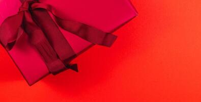banner Red gift box with dark red bow and ribbon on red background photo