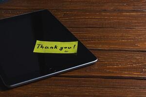 Yellow note with the word thank you on the tablet screen on the table photo