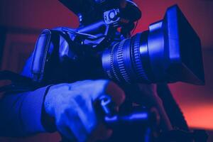 Professional Videographer Capturing a Moment With a Large Camera Under Colorful Lighting at Dusk photo