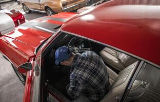 Man Working on a Classic Red Car Inside a Vintage Automobile Collection Garage photo