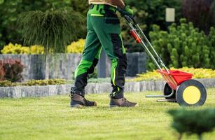 Gardener Using a Lawn Spreader to Maintain Green Grass in a Well-Kept Garden During Daylight photo