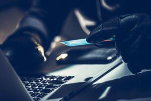 Criminal Using a Computer to Commit Fraud With a Credit Card at Night in a Dimly Lit Room photo
