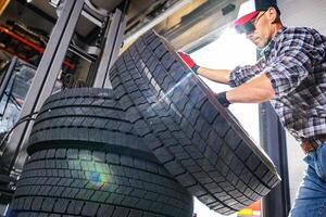 A Worker Stacks Large Tires in a Workshop as Sunlight Streams Through Shop Doors photo