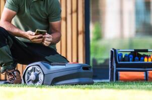 Man Operating a Robotic Lawn Mower While Managing Landscaping Tools in a Modern Backyard Setting photo