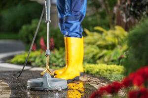 Person Using a High-Pressure Washer on a Garden Path Surrounded by Vibrant Plants in Sunny Weather photo