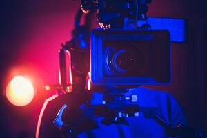 A Filmmaker Operates a Professional Camera Under Vibrant Colored Lights in a Studio Setting photo