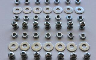 Perfectly even rows of steel shiny nuts, bolts and washers on a white surface photo