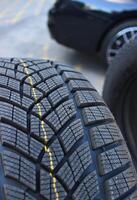 Snowflake pictogram to show wear level on new winter tire in front of a defocused car at tire service. Seasonal tire change stock image. Design of non studded winter tires photo