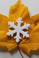 A toy snowflake covers a bright yellow autumn leaf. Symbols of the end of autumn and the beginning of winter photo