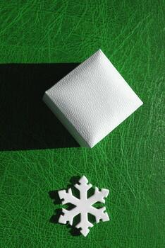 Small Gift Case And Artificial Snowflake On Green Patterned Surface. Vertical Stock Photo For Illustration Of Modest Presents For New Year and Christmas