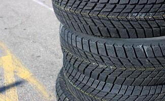A set of four new winter tires are stacked on asphalt before the seasonal tire change. Same tread pattern tires detailed image photo