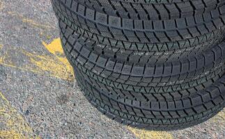 Identical winter tires with aggressive tread patterns are stacked on the highway. Same studless tires stock photo