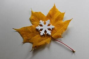 White Snowflake Figurine On A Bright Yellow Leaf On White Surface. Changing Seasons Stock Photo