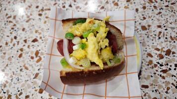 Scrambled egg breakfast sandwich with sausage, green onions, and onions on a soft bun, served on a patterned countertop, perfect for a quick morning bite. photo