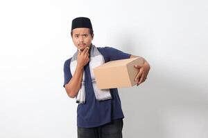 Portrait of confused Asian muslim man wearing sarung scarf and skullcap thinking with hand on chin. Isolated on white background photo