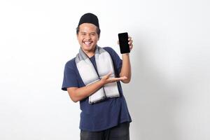 Portrait of excited Asian muslim man wearing sarung scarf showing blank screen mobile phone mockup while pointing and presenting product. Social media concept. Isolated image on white background photo