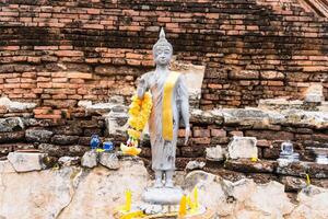Serene Buddha Figure Draped in Yellow Garland, Set Against a Rustic Brick Background at Ayutthaya, Thailand. photo