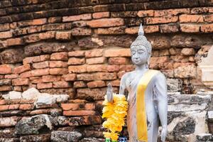 Serene Buddha Figure Draped in Yellow Garland, Set Against a Rustic Brick Background at Ayutthaya, Thailand. photo
