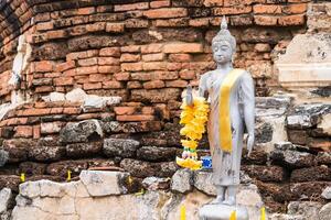 Serene Buddha Figure Draped in Yellow Garland, Set Against a Rustic Brick Background at Ayutthaya, Thailand. photo