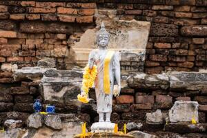 Serene Buddha Figure Draped in Yellow Garland, Set Against a Rustic Brick Background at Ayutthaya, Thailand. photo