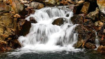 A small waterfall with clear water flows rapidly over large natural rocks, creating an enchanting and calming view. photo