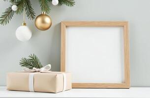 Minimalist holiday scene featuring a beige wrapped gift with a white ribbon, blank wooden frame, and fir branches adorned with white and gold baubles. Merry christmas and Happy New Year photo