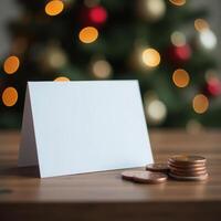 Blank holiday card displayed on wooden table with christmas tree and coins in background. concept of banking, finance, business photo