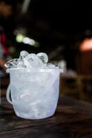 Transparent plastic bucket with ice cube on a table photo