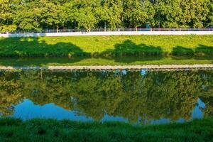 The river flows through the city. On the calm surface of the river banks are reflected. Slovak river Nitra on a bright sunny day. photo