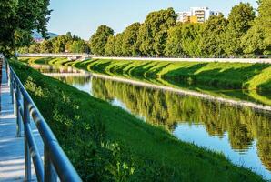 The river flows through the city. On the calm surface of the river banks are reflected. Slovak river Nitra on a bright sunny day. photo