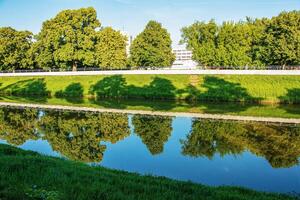 The river flows through the city. On the calm surface of the river banks are reflected. Slovak river Nitra on a bright sunny day. photo