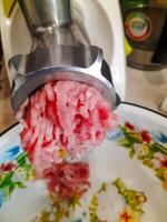 The process of grinding meat in the kitchen using a meat grinder. Preparing raw meat for cooking. Selective focus. photo