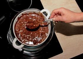 Powdered sugar, cocoa butter and grated cocoa in a container for making chocolate are heated in a water bath. photo