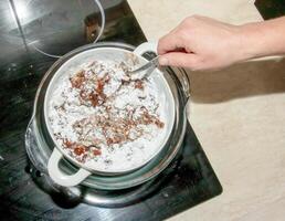 Powdered sugar, cocoa butter and grated cocoa in a container for making chocolate are heated in a water bath. photo