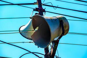 Loud Speaker or vintage white horn speaker on the pole. For public relations in the community. With wires, cables and blue skies as the background. photo