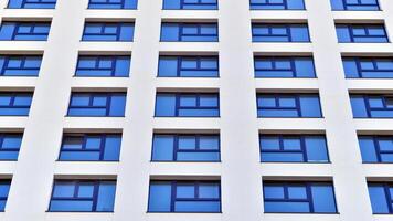 Modern high-rise apartment building in white, stand tall against a blue sky, exemplifying innovative urban architecture with sleek, angular designs. photo