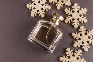 Chic bottle of perfume with a gold cap on a brown leather with Christmas golden snowflakes. An empty mockup of a non branded bottle. top view. photo