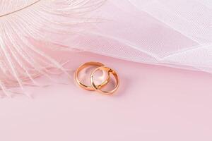 Two classic gold rings on a pink background with part of a white bridal veil with a delicate airy feather. A copy space. design, postcard, invitation. photo