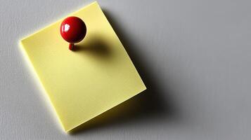 A bright yellow sticky note is anchored by a red push pin, creating a playful contrast photo
