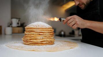 A chef expertly caramelizes sugar on a tall stack of pancakes using a kitchen torch photo