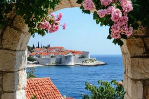 Redroofed houses frame an array of vibrant pink flowers that overlook calm waters, beautifully blending the charm of historical architecture with the serene allure and captivating beauty of nature photo