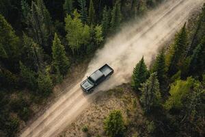 An aerial shot shows a black pickup truck navigating a winding dirt road through a lush green forest, stirring up dust and creating a dramatic scene that evokes a sense of adventure photo