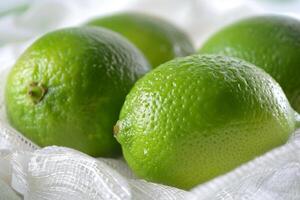 Close-up of four fresh green limes placed on a white cloth background, highlighting their vibrant color. photo