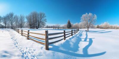 A serene winter scene featuring a snowcovered wooden fence leading into a vast snowy field under a clear blue sky photo