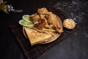 Chicken Drumstick with French Fries, Toasted Bread and Salad served in wooden plate isolated on dark background side view of bangladeshi fast food photo