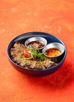 Korean Grilled Pork Belly Rice Bowl with dipping sauce with herbs isolated on orange background side view of fast food meal photo