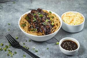 Teriyaki Grilled Chicken Noodles with green onion, spicy sauce, cabbage salad and fork served in bowl isolated on grey background side view of japanese food photo