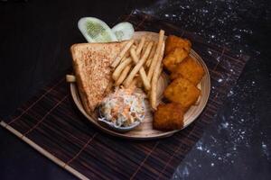Chicken Nuggets with tomato, onion, lettuce leave, capsicum, french fries and salad served in wooden plate isolated on dark background side view of bangladeshi fast food photo