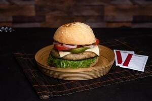 Classic Chicken Cheese Burger include tomato, onion, lettuce leave, capsicum and sauce served in wooden plate isolated on dark background side view of bangladeshi fast food photo