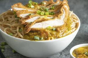 Katsu Chicken Noodles with potato curry, green onion and fork served in bowl isolated on grey background closeup side view of Asian food photo